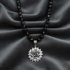 Necklace with a silver pendant on a black beaded chain against a gray fabric background