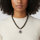 Woman wearing a necklace with a decorative pendant against a neutral background