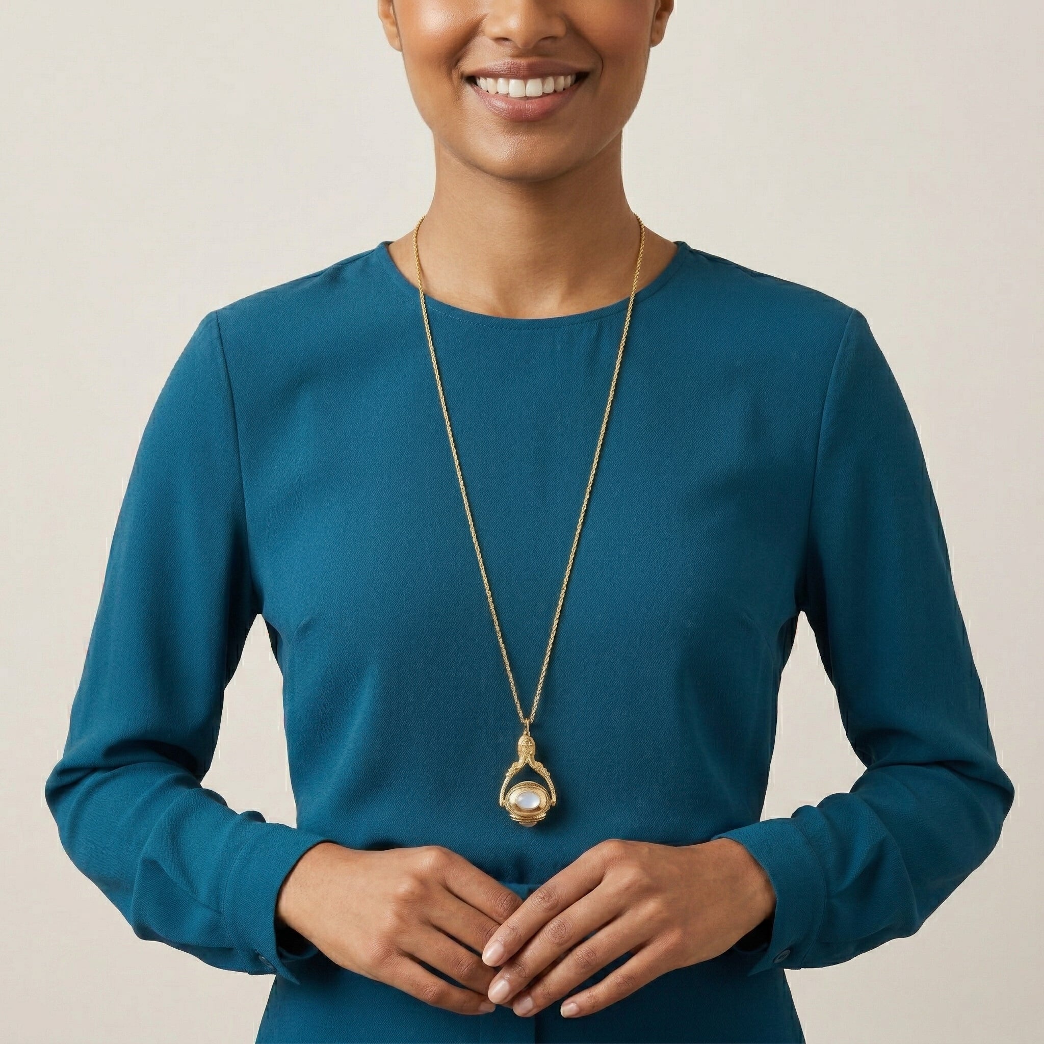 Woman wearing a blue dress and gold necklace with a spinner gemstone pendant against a beige background