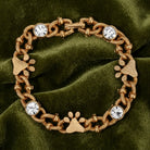 Gold tone Paws & Crystal Link Bracelet resting on dark olive green fabric