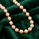 Round Champagne Faux Pearl Beaded Necklace resting on dark green fabric