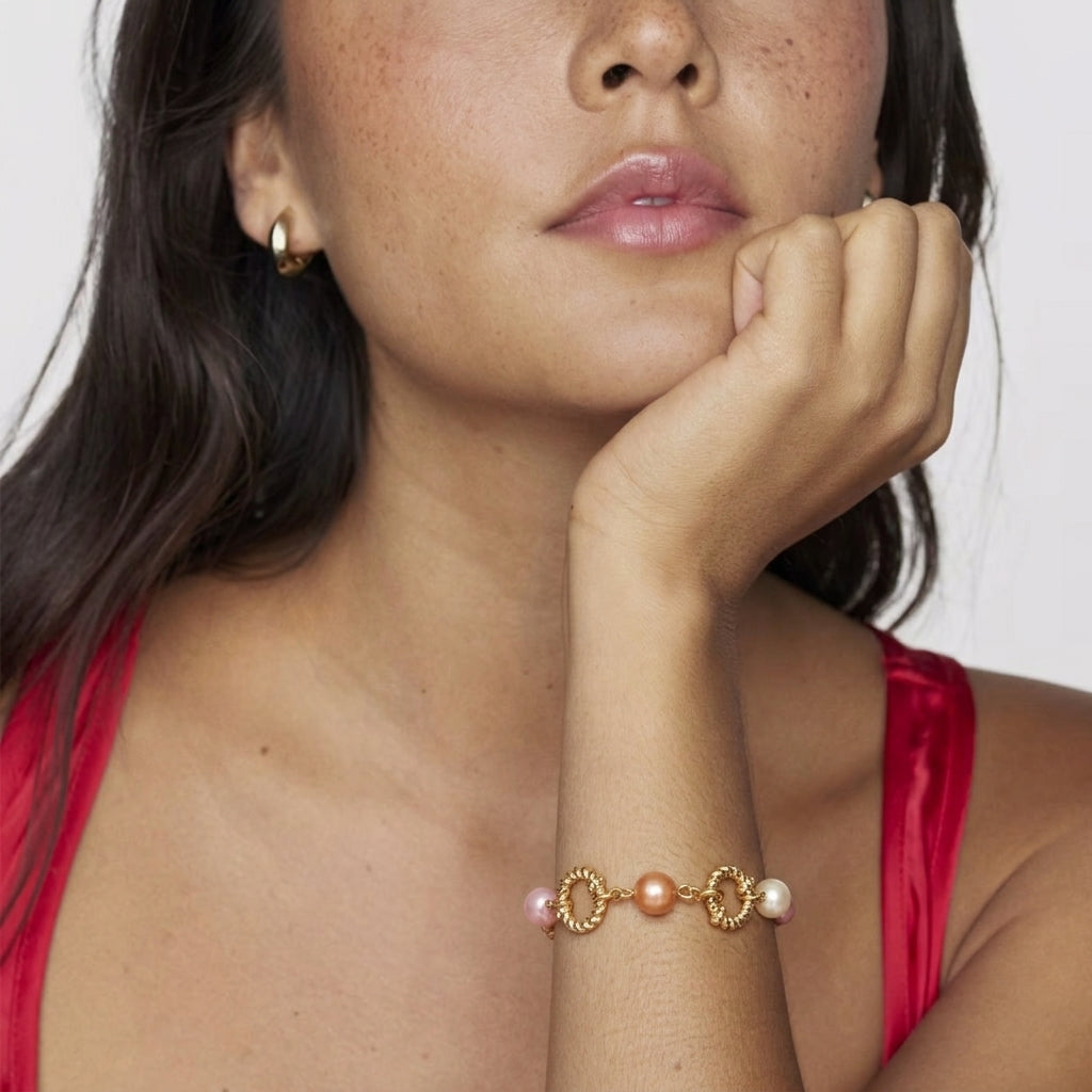 Woman wearing a gold bracelet with pink beads and pearls on a white background