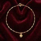 Gold bracelet with a heart charm on a burgundy velvet background