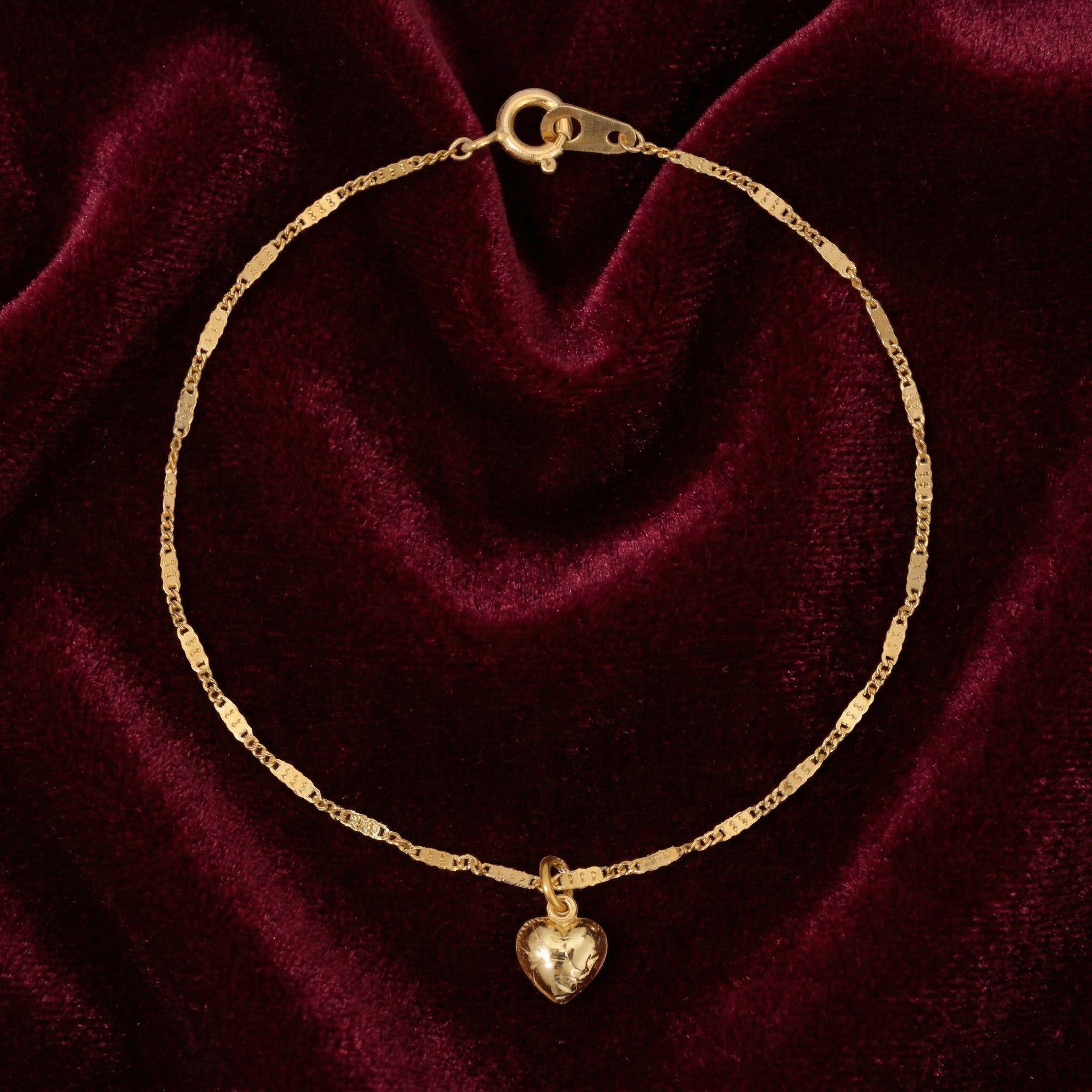 Gold bracelet with a heart charm on a burgundy velvet background