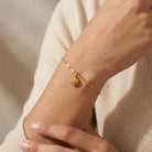 Gold bracelet with a heart charm on a wrist against a neutral background