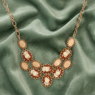 Gold tone cameo rose bib necklace with peach colored stones resting on olive green fabric