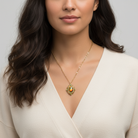 Woman wearing a gold necklace with a green pendant against a neutral background
