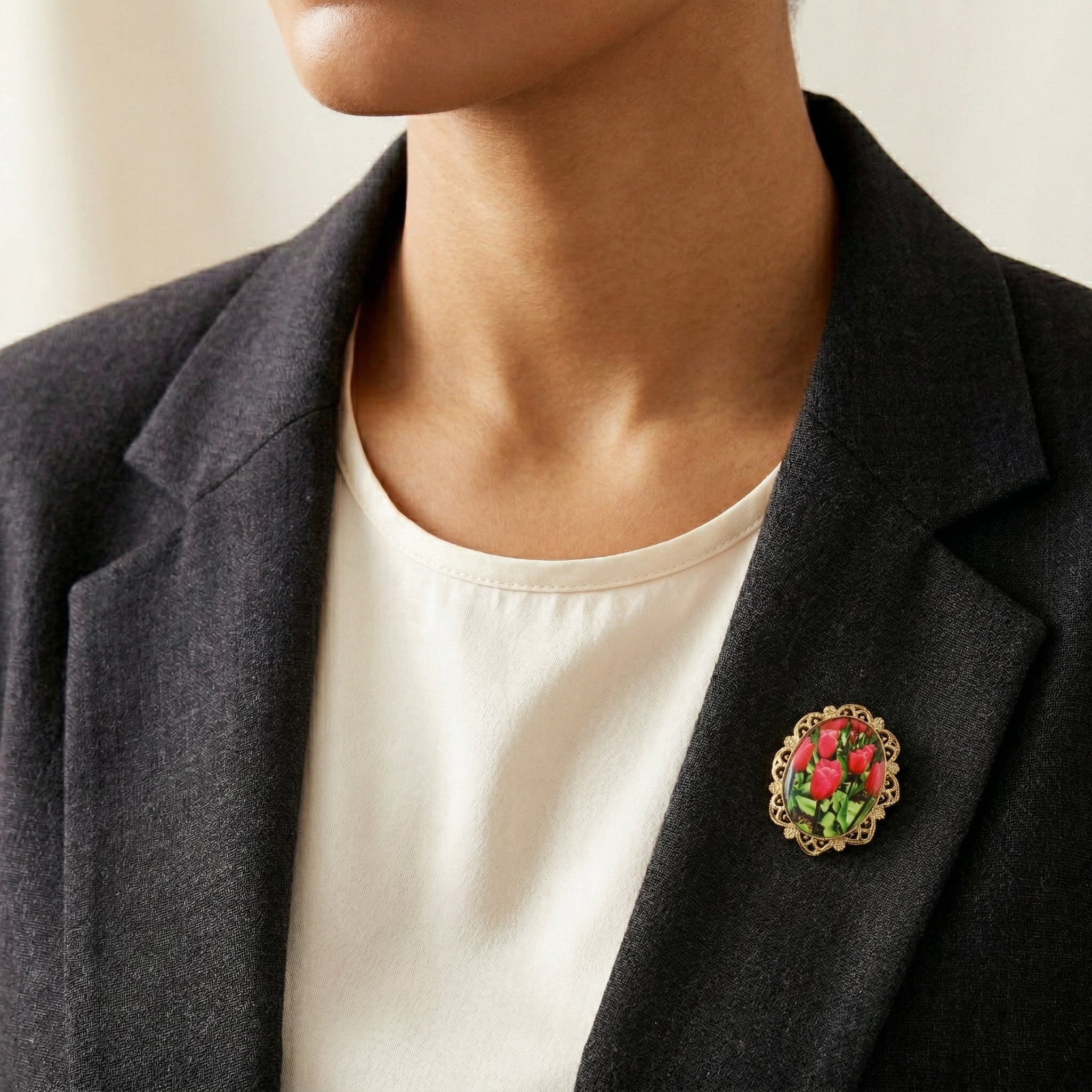 Person wearing a dark blazer with a floral tulip brooch on a neutral background