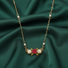 Necklace with floral design and faux pearls with a red rose on the pendant on a green fabric background
