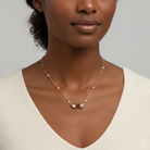 Woman wearing a delicate gold necklace with small faux pearls with floral pendant on a neutral background