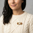 Woman wearing a cream sweater with a decorative floral brooch on a gray background