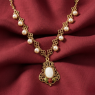 Gold necklace with pearls and a decorative pendant with a rose attached beneath on a red fabric background