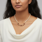 Woman wearing a faux pearl necklace and a floral pendant with a white top against a neutral background
