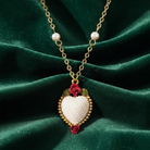 Necklace with a heart-shaped pendant filled with small, decorative faux pearls and red roses on a green fabric background