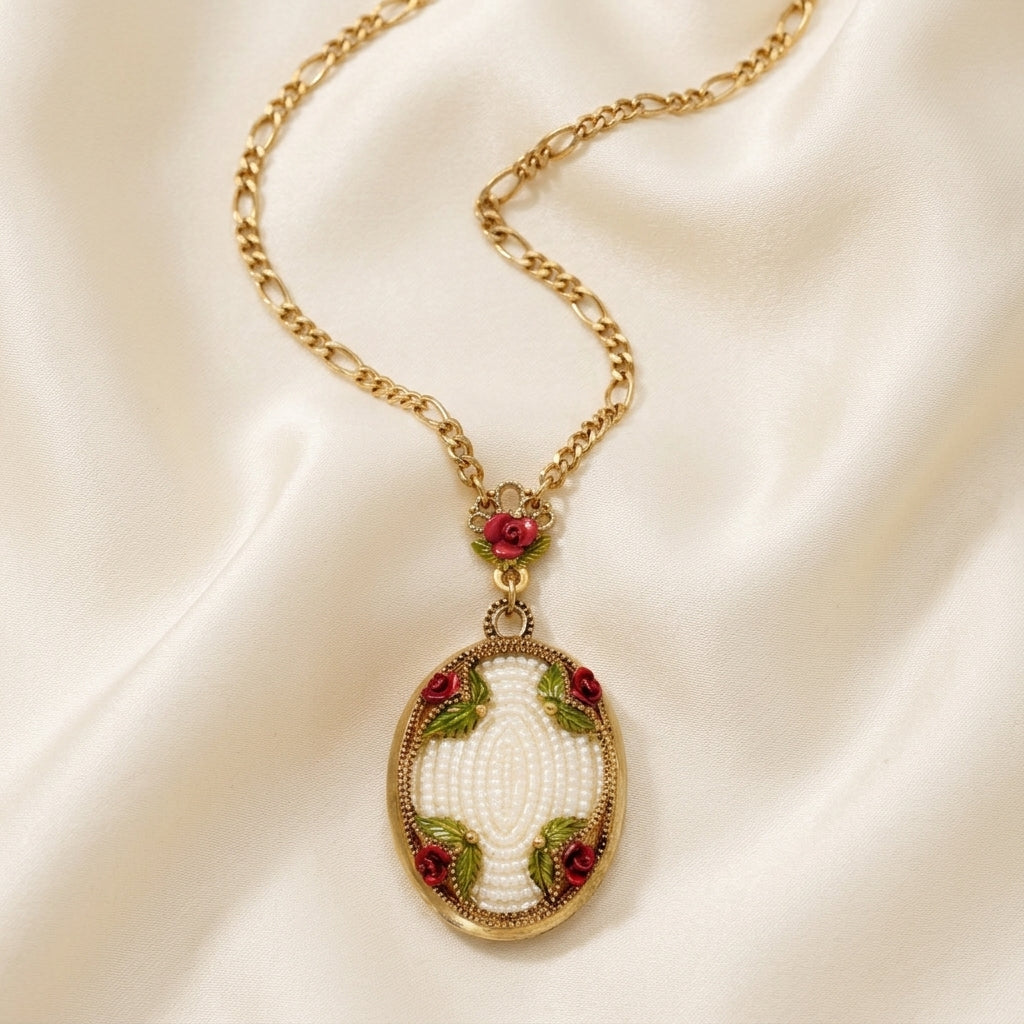 Gold tone chain necklace with a faux pearl pendant that has rose designs resting on cream colored satin fabric