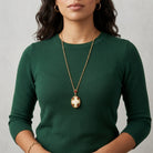 Woman in a green top wearing a gold tone chain necklace with a faux pearl pendant that has rose designs