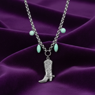 Necklace with cowboy boot pendant and turquoise beads on a purple fabric background