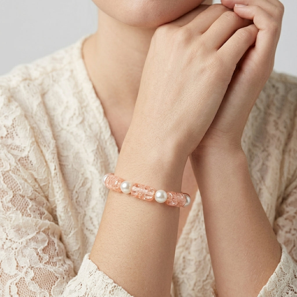 A close-up of a person wearing a Peach Cracked Glass & White Faux Pearl Beaded Bracelet on the wrist, styled with a cream lace top.