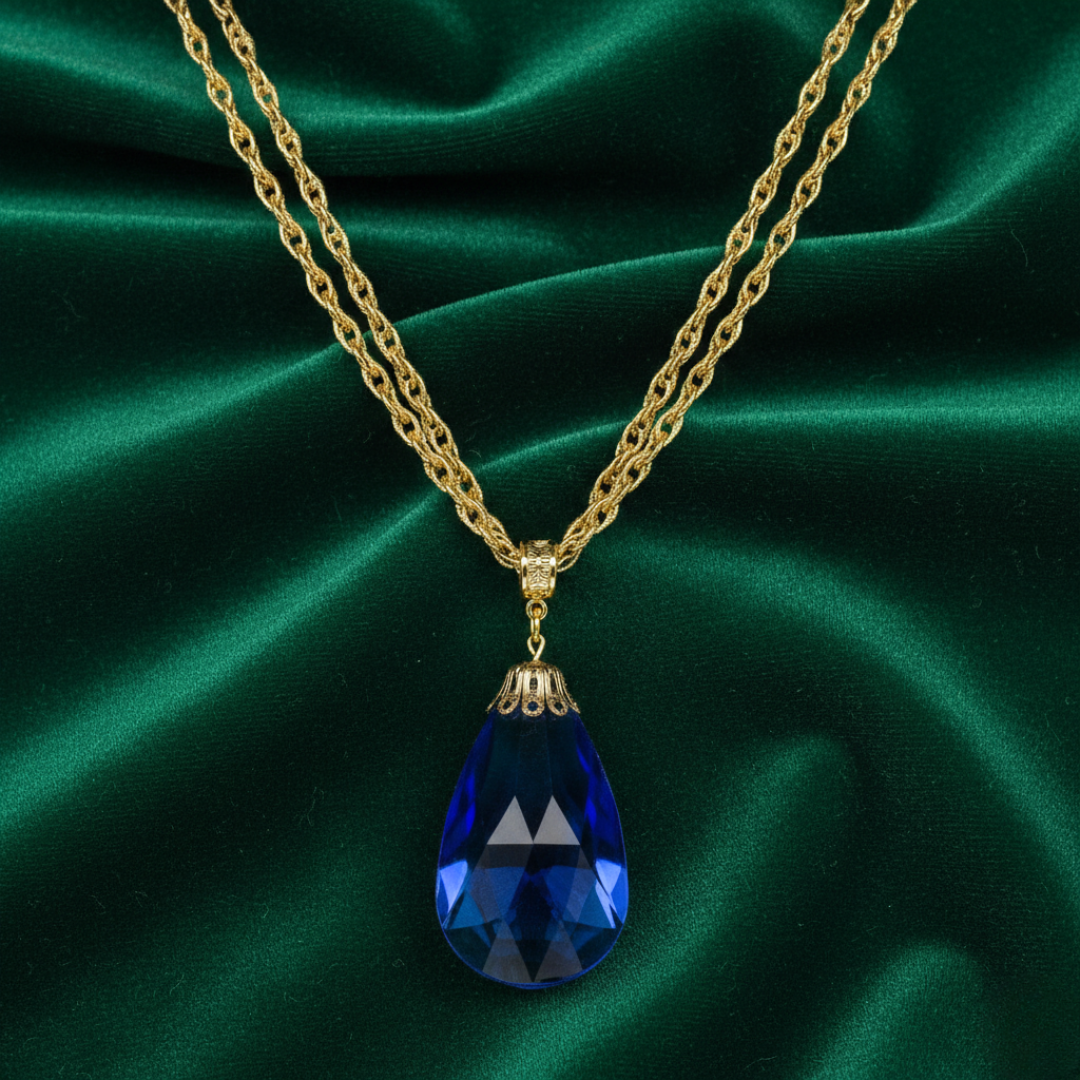 Gold necklace with a blue teardrop pendant on a green satin background