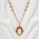 Red carnelian ivory rose pendant that has topaz stone accents on a gold tone chain resting on white satin fabric
