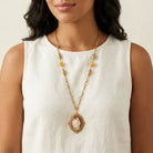 Woman in a white top wearing a red carnelian ivory rose pendant that has topaz stone accents on a gold tone chain