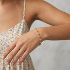 A delicate Classic Golden Heart Link Chain Bracelet worn on a woman's wrist. The model is wearing a light floral print camisole against a soft, light gray background.