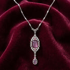 Silver tone purple stone drop pendant necklace resting on dark magenta fabric