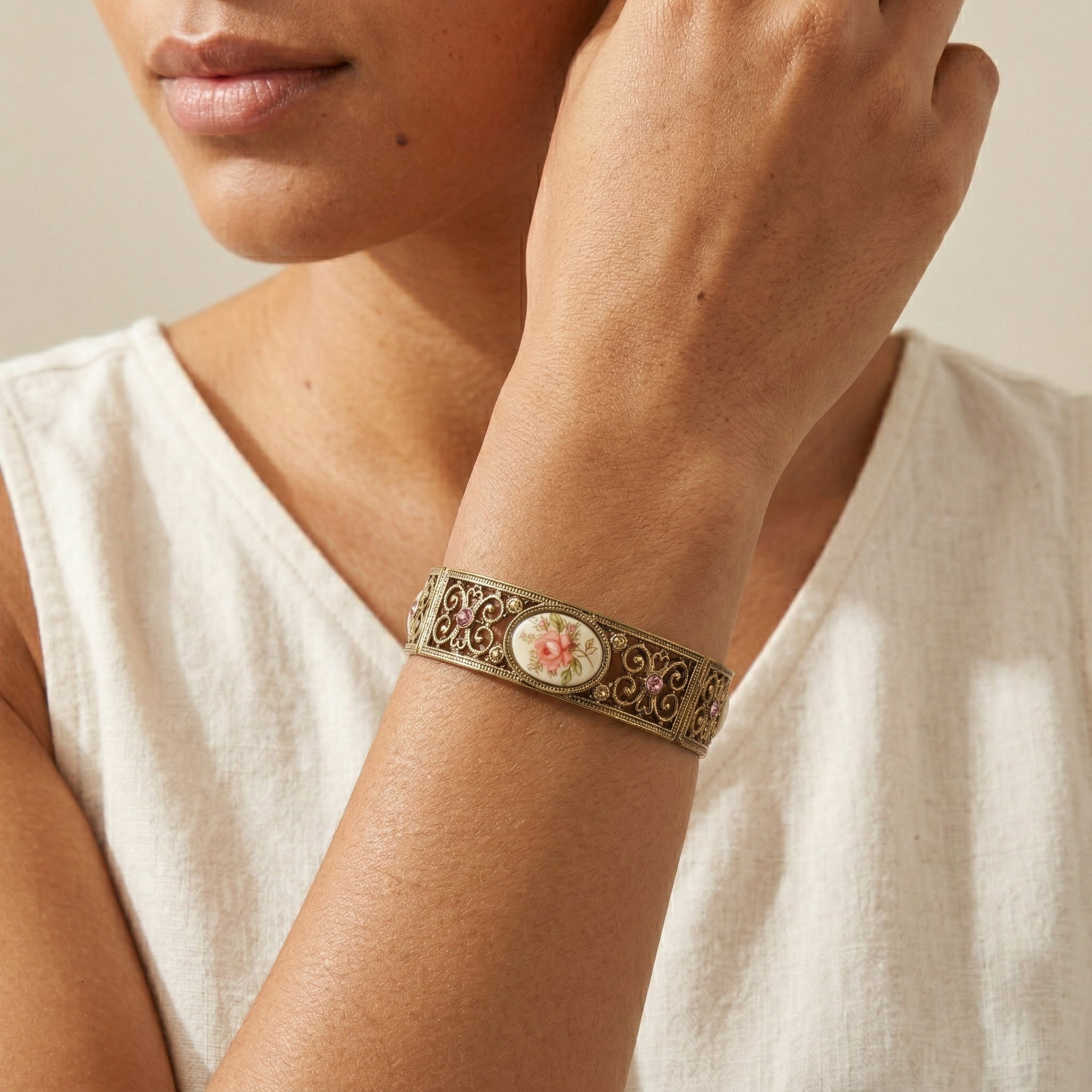 Close-up of a person wearing a decorative bracelet with pink crystals and floral design on a neutral background