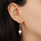 A close-up of a model's ear wearing a delicateRound Pink Faux Pearl & Crystal Drop Earring