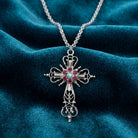 Silver tone cross necklace with purple crystals resting on blue fabric