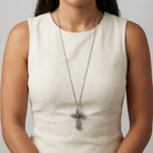 Woman in a neutral outfit wearing a silver tone long cross pendant necklace with purple crystal accents