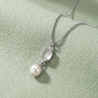 Translucent Flower Engraved Stone & Faux Pearl Drop Pendant Necklace displayed on a soft light green textured fabric background.