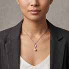 A close-up of a model wearing a Translucent Flower Engraved Stone & Faux Pearl Drop Pendant Necklace, styled with a dark gray blazer and white top.