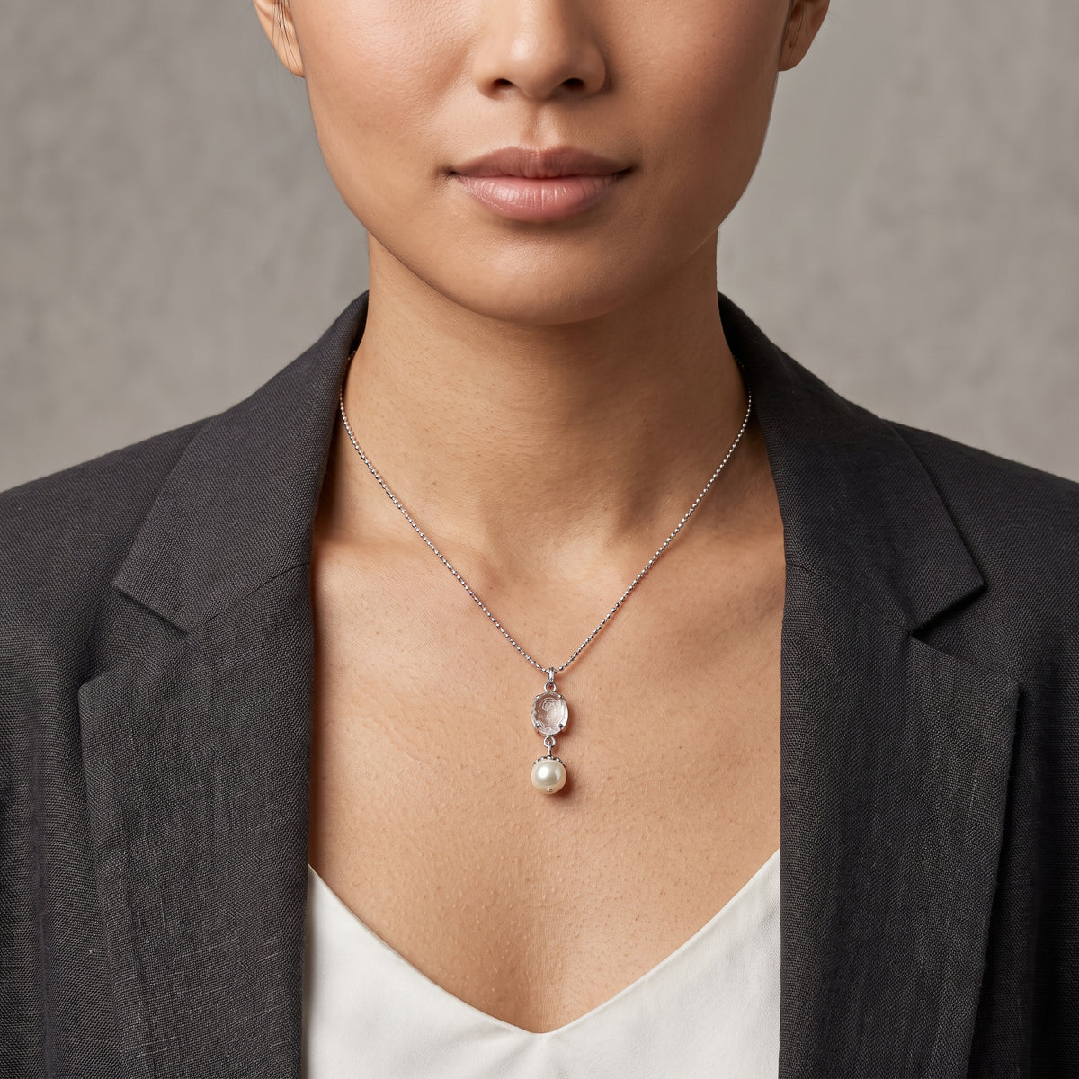 A close-up of a model wearing a Translucent Flower Engraved Stone & Faux Pearl Drop Pendant Necklace, styled with a dark gray blazer and white top.