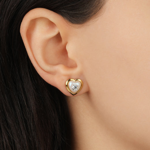 Gold heart-shaped earring with a clear gemstone worn by a person.