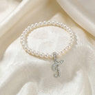 Pearl bracelet with a silver letter 'J' charm on a white fabric background