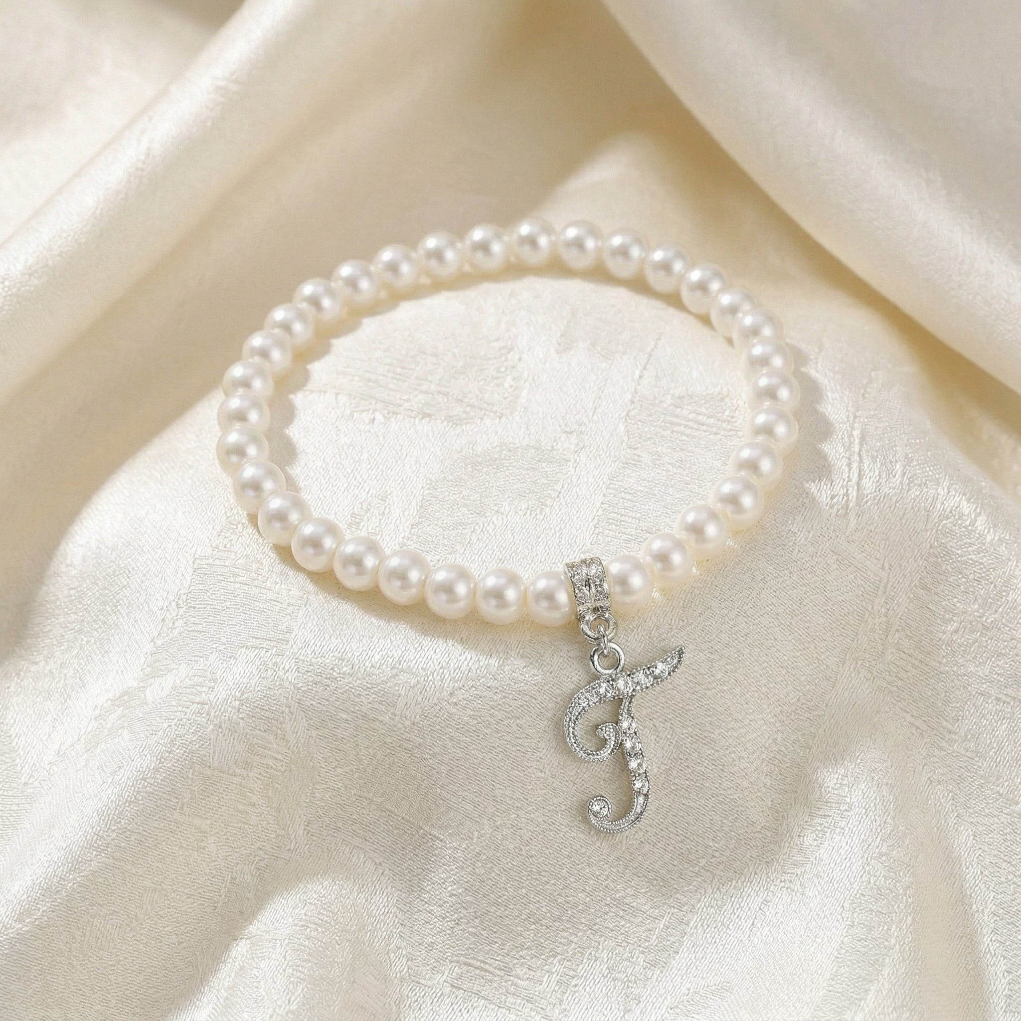 Pearl bracelet with a silver letter 'J' charm on a white fabric background