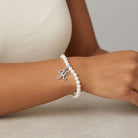 Pearl bracelet that has an initialed charm with a silver clasp on a wrist against a neutral background