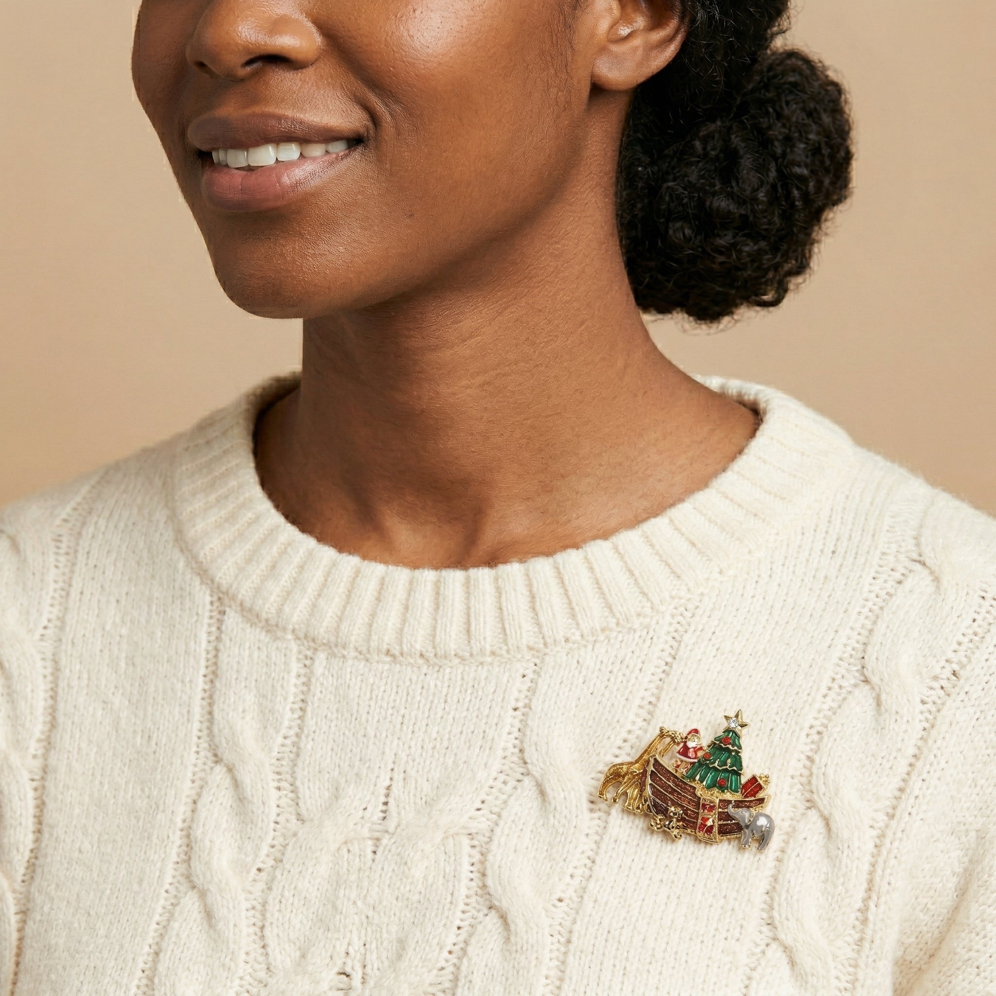 Woman wearing a cream sweater with a decorative Santa Claus sleigh and Christmas tree brooch on a beige background