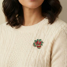 Person wearing a cream sweater with a decorative holiday ornament brooch on a neutral background