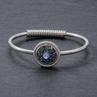 Blue pave crystal silver tone spring hinge bracelet resting on a gray stone surface
