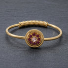 Purple pave crystal gold tone spring hinge bracelet resting on a gray stone surface