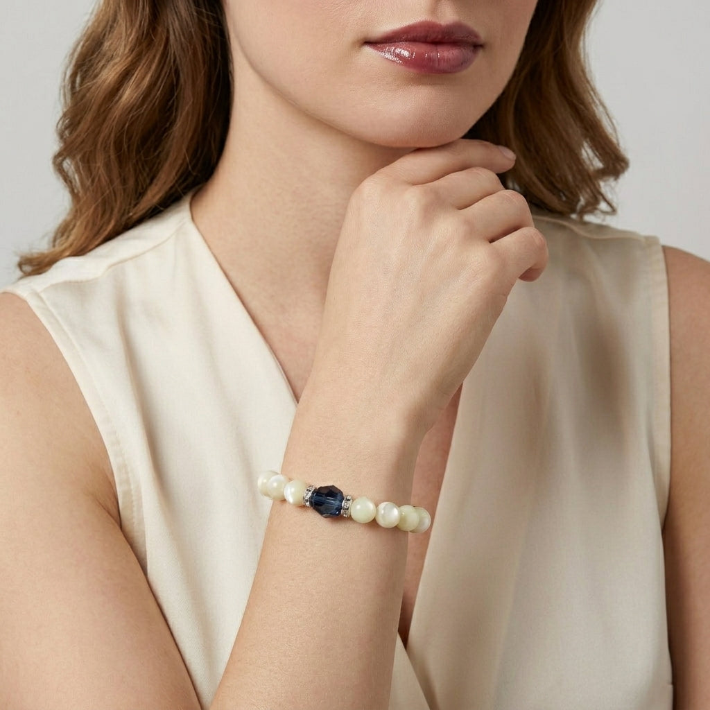 Woman wearing a pearl bracelet with a Montana Blue bead on a plain background