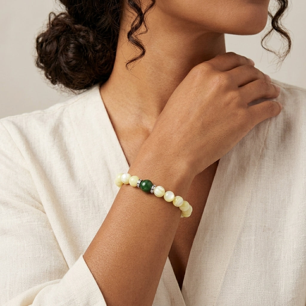 Woman wearing a pearl bracelet with green gemstone on a neutral background