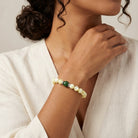 Woman wearing a pearl bracelet with green gemstone on a neutral background