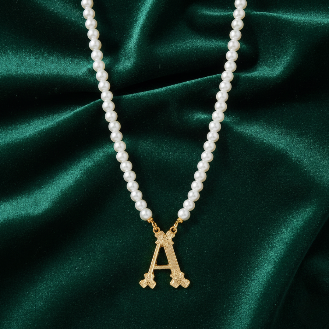Faux pearl necklace with a gold 'A' initialed pendant on a green fabric background. 