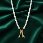 Faux pearl necklace with a gold 'A' initialed pendant on a green fabric background. 