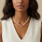Woman wearing a pearl necklace with a gold pendant featuring the letter 'A'.