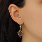 A close-up of a model's ear wearing Gold Filigree & Diamond Shaped Brick Red Gemstone Drop Earrings