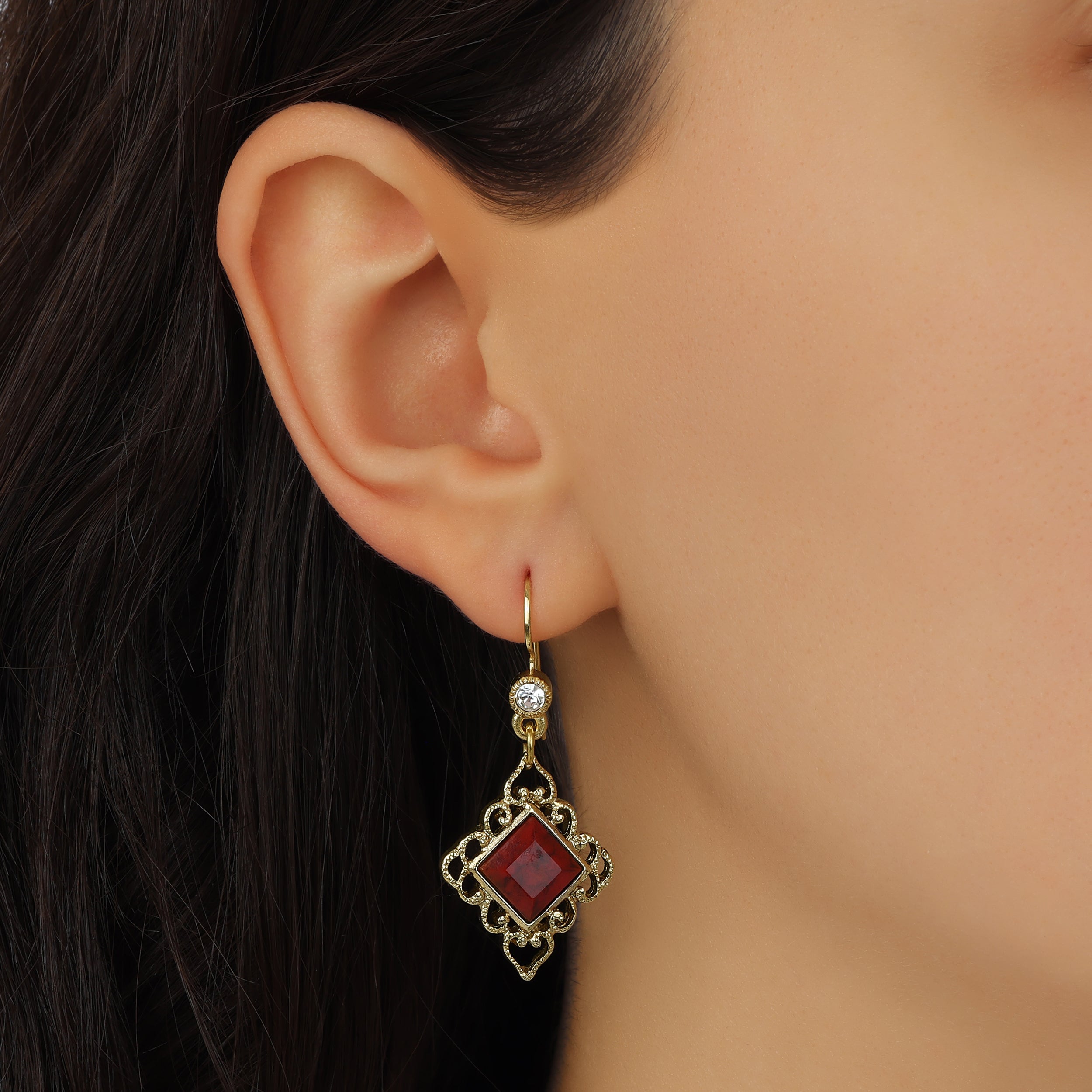 A close-up of a model's ear wearing Gold Filigree & Diamond Shaped Brick Red Gemstone Drop Earrings